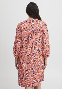 Rochie florală în nuanțe de roz, portocaliu și bleumarin. Are mâneci lungi, puffate, un croi lejer și detalii plisate la spate. Material ușor, texturat.