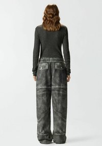 Maglia grigia a maniche lunghe a coste con lavorazione a maglia strutturata e jeans neri a vita alta con gambe larghe, dettagli patchwork e cuciture bianche.