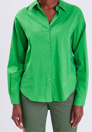 Groen overhemd met knopen, gemaakt van gladde stof, met een kraag en lange mouwen. De zoom is licht gebogen; gecombineerd met groene broek met een patroon.