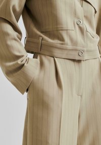 Beige randig kostym med en prydlig passform. Har ett midjebälte, synliga knappar och en texturerad tyg. Korta ärmar och strukturerad design.