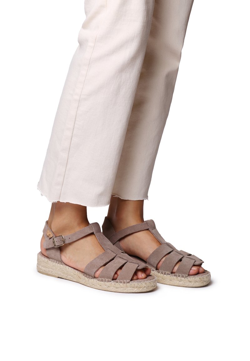 Sandalias de ante marrón con punta abierta y múltiples correas, combinadas con pantalones cortos blancos y una suela estilo yute.