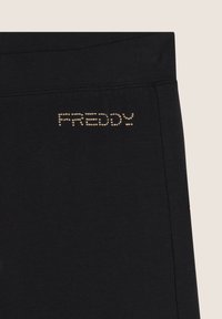 Pantalones cortos deportivos negros hechos de una tela suave, con "FREDDY" en puntos dorados en la cintura y una etiqueta de acento roja.