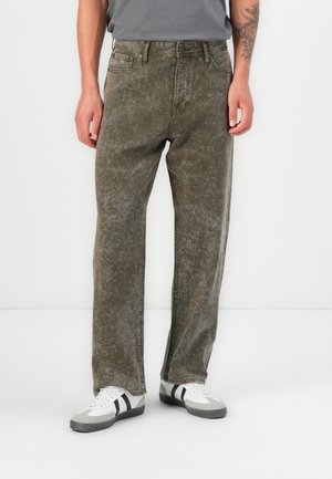 Baggy, olivengrønne jeans med en falmet tekstur, fem-lomme-design og synlige sømmer, kombinert med grå og hvite joggesko.