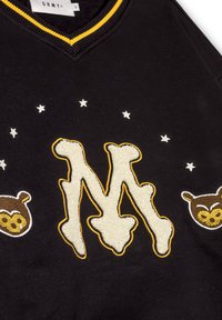 Sudadera negra con escote en V y acentos amarillos. Presenta una "M" bordada y dos ilustraciones de osos, rodeadas de estrellas blancas.