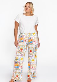 Weißes Kurzarmoberteil, kombiniert mit bunten, gemusterten weiten Hosen, die Früchte und Orte wie „Hawaii“ und „Los Angeles“ zeigen.
