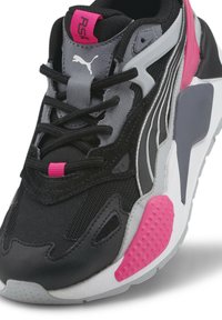 Gros plan d'une basket Puma RS noire, grise et rose avec un laçage à l'avant et des accents roses texturés sur la semelle et le talon.
