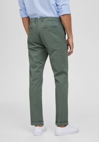 Zelené bavlněné kalhoty mají volný střih, ohrnuté lemy a zadní kapsy s knoflíkovými zapínáními, kombinované s bílými teniskami.