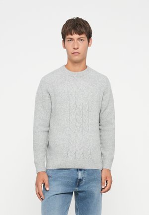 Lysegrå strikkegenser med kabelmønster, rund hals og lange ermer, kombinert med blå jeans. Mykt, strukturert stoff.