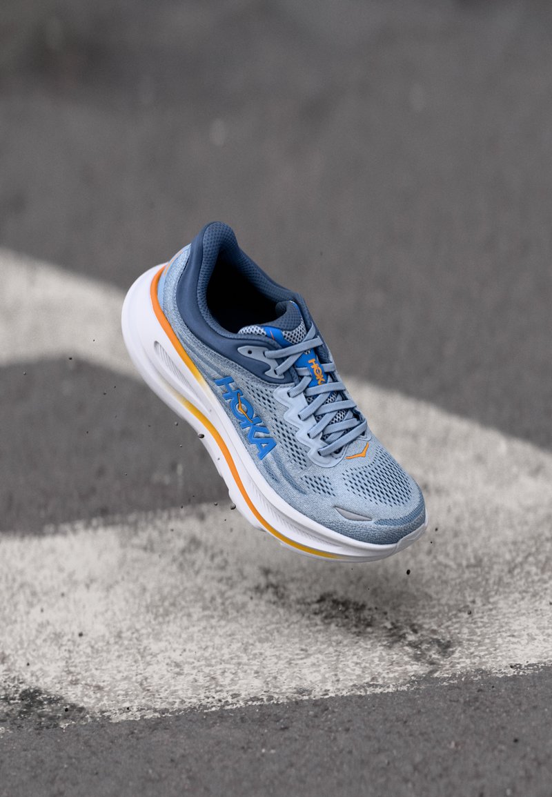 Baskets de course bleu clair avec tige en mesh respirant, col rembourré et semelle blanche caractérisée par des accents orange et jaune.
