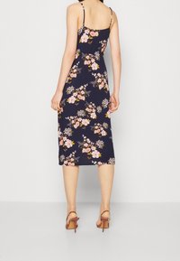 Blommig midi-klänning med tunna remmar; marinblå bakgrund med rosa och vita blommor; lättviktig tyg; kombinerad med bruna klacksandaler.