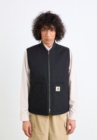 Schwarze ärmellose Weste mit Reißverschluss, zwei Vordertaschen und Logo-Patch. Hergestellt aus strapazierfähigem Material und einem klaren, minimalistischen Design.