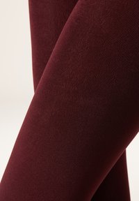 Bordeaux leggings med en glat, mat overflade og en tætsiddende design, der viser et ensartet, strækbart stof uden synlige sømme.