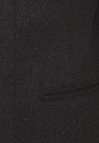 Cappotto in lana grigio scuro con finitura testurizzata. Presenta una tasca frontale singola e un design tradizionale del colletto.