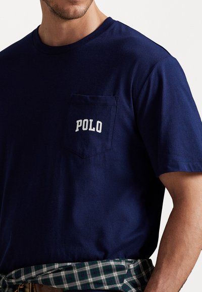 Granatowa bawełniana koszulka z okrągłym dekoltem, z kieszonką na lewej piersi oraz białym logo "POLO". Materiał ma gładką fakturę.