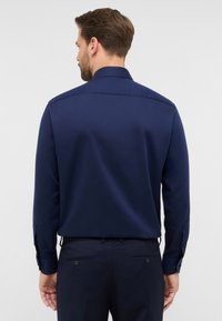 Camicia a maniche lunghe navy con colletto classico, texture liscia e polsini con bottone. Presenta una vestibilità sartoriale con un design posteriore pulito.