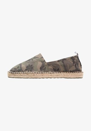 Espadrille camouflage verte avec une tige en tissu, une semelle en jute et une bordure tissée. Le design présente des motifs floraux sur un fond texturé.
