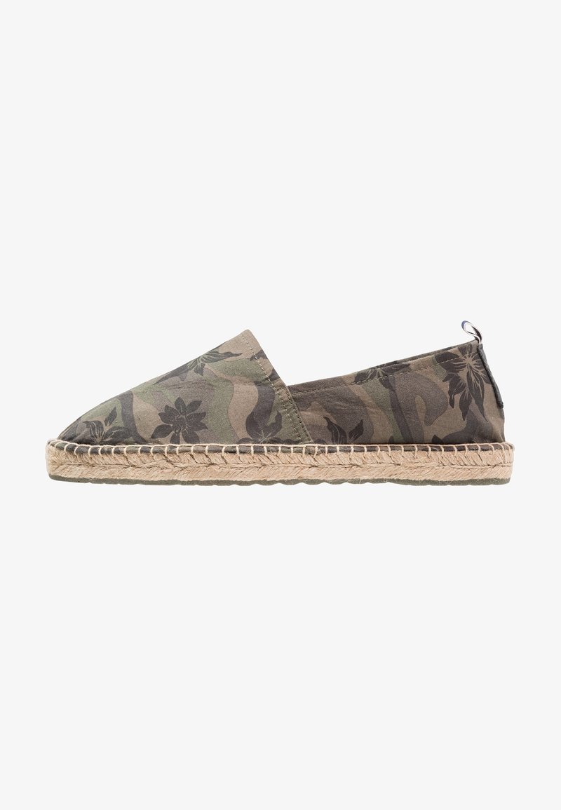 Espadrille camouflage verte avec une tige en tissu, une semelle en jute et une bordure tissée. Le design présente des motifs floraux sur un fond texturé.