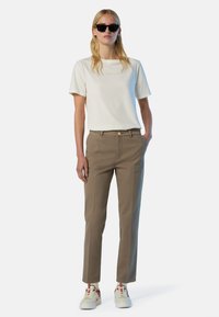 Camiseta de algodón color beige claro con mangas cortas, combinada con pantalones verde olivo, con un corte clásico y un botón en la cintura. Zapatillas blancas.