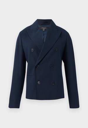 Blazer bleu marine à double boutonnage avec revers, deux poches avant et six boutons recouverts de tissu. Fabriqué en matériau lisse et structuré.