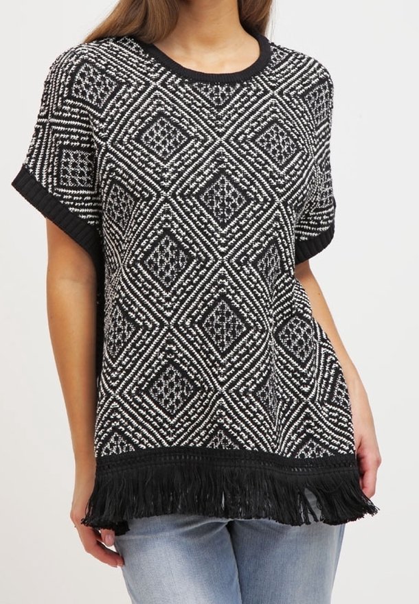 Haut en tricot à motifs noir et blanc avec un design en losanges, manches courtes, col côtelé et ourlet frangé. Porté sur un denim clair.