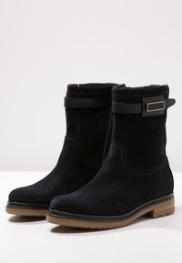 Svarta mocka ankelstövlar med rund tå, dragkedja på sidan, läderrem som accent och en strukturerad tanfärgad sula.