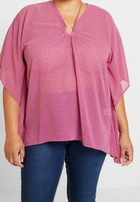 Haut rose à motifs avec un col en V, des manches chauve-souris et un col froncé. Présente un imprimé géométrique dans des teintes plus claires. Matière en mélange de coton.