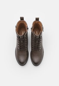 Un par de botas de cuero marrón oscuro, con cordones y cremallera lateral, vistas desde arriba sobre un fondo blanco.