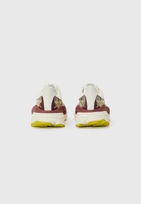 Rote und weiße Sneakers mit strukturierten Netzpaneelen, gelben Gummisohlen und floralen Stickereien an den Fersenteilen.