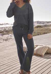 Set di loungewear a coste grigio scuro composto da un top a maniche lunghe con scollo a V e pantaloni con coulisse con dettagli dorati, ambientato su uno sfondo naturale.
