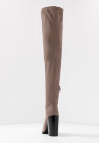 Bota de ante marrón hasta la rodilla con un diseño elegante, punta redonda y un tacón negro grueso. Cuenta con un cierre lateral para facilitar el uso.