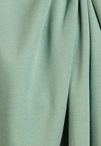 Textuurstof in lichtgroen met plooien, die een gladde oppervlakte en zachte uitstraling toont. Ideaal voor kleding of bekleding.