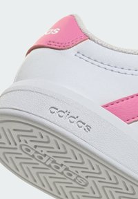 Tenisky Adidas s bílým koženým svrškem s růžovými akcenty, texturovanými hranami a vzorovanou gumovou podrážkou, zobrazující logo značky.