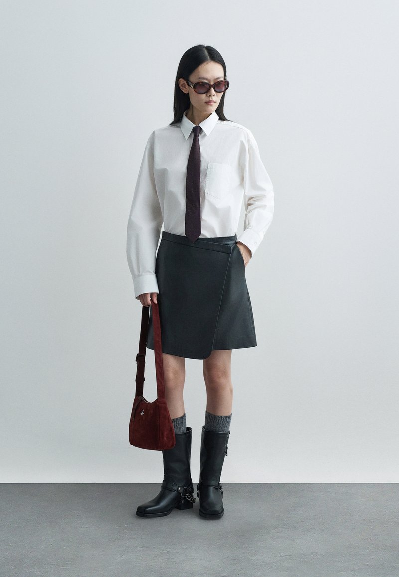 Hvid skjorte med lange ærmer, mørkegrå omslagsskjørt, sorte knæhøje støvler, grå strømper og maroon håndtaske. Mørke solbriller som tilbehør.