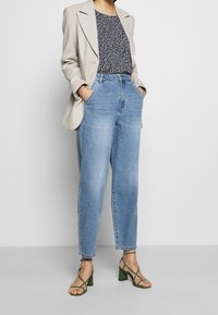 Lys grå blazer over en mørk blomsterprint top, parret med højtaljede lyseblå jeans og grønne strappy blokhælsandaler.