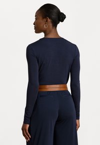 Marineblauwe longsleeve top met ronde halslijn, gecombineerd met een bruine meerlagige leren riem. De stof lijkt glad en aansluitend.