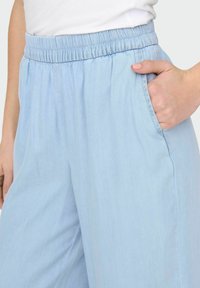 Pantalons de couleur bleu clair, amples et fabriqués à partir d'un matériau doux et léger. Dotés d'une taille élastique et de poches latérales.