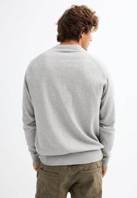 Suéter gris de cuello redondo en suave tejido de punto, con dobladillos acanalados y mangas ranglán. Diseño sencillo sin patrones o acentos visibles.