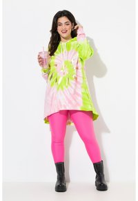 Sudadera con capucha de tie-dye en rosa y verde con acentos dorados, combinada con leggings rosa brillante y botas de tobillo negras con tachuelas.