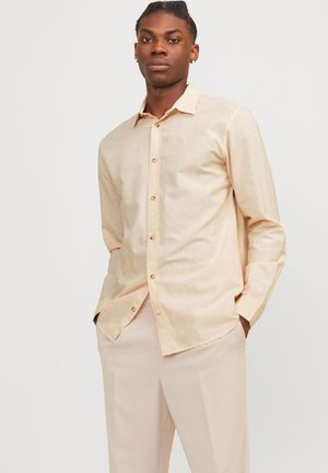 Camicia beige a maniche lunghe realizzata in tessuto leggero, con chiusura a bottoni, colletto e una vestibilità leggermente rilassata. Texture semplice e liscia.