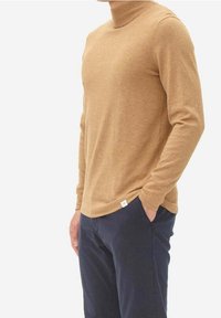 Khaki long-sleeve turtleneck sweater in a lightweight knit, featuring a smooth texture and relaxed fit, paired with dark navy pants.