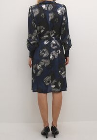 Marineblauwe jurk met abstract grijs en witte patroon, lange mouwen, een ceintuur in de taille en een zijnaad, gemaakt van een lichte stof.