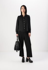 Black button-up shirt with textured fabric, long sleeves, and white buttons, paired with black wide-leg pants and chunky black heeled shoes.