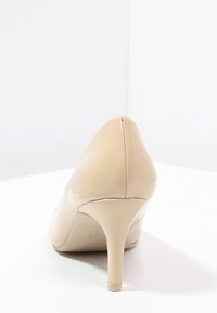 Beigen värinen patenttinahkainen korkokengä, jossa on kapea kärki ja ohut 10 senttimetrin korko. Tasainen pinta, jossa saumatasku takana.