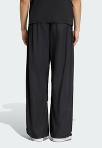 Mustat leveälahkeiset housut, jotka on valmistettu kevyestä materiaalista, joissa on joustava vyötärö ja sileä pinta, yhdistettyinä valkoisiin lenkkareihin.