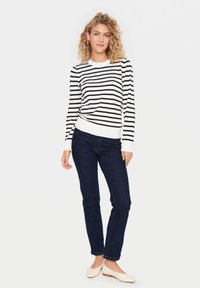 Pull à rayures noir et blanc avec un col rond et des poignets côtelés, associé à un jean bleu foncé et des chaussures plates beiges. Design simple et ajusté.