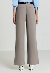 Pantaloni a gamba larga in un tessuto grigio chiaro, caratterizzati da una texture liscia, due tasche posteriori e una cintura nera, abbinati a tacchi bianchi.