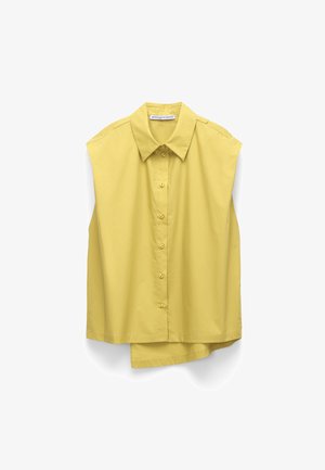 Bezrekawna żółta koszula na guziki z ostrym kołnierzykiem i lekko asymetrycznym dołem, wisząca na białym tle.