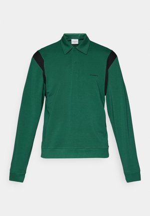 Roheline pikkade varrukatega polo särk, millel on must aksent vasakul õlal. Omab kraed, kahte nupuvajutust ja pehmet tekstuuri.