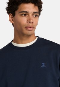 Felpa blu navy con colletto a coste, caratterizzata da un piccolo logo Timberland ricamato sul petto, realizzata in tessuto morbido.