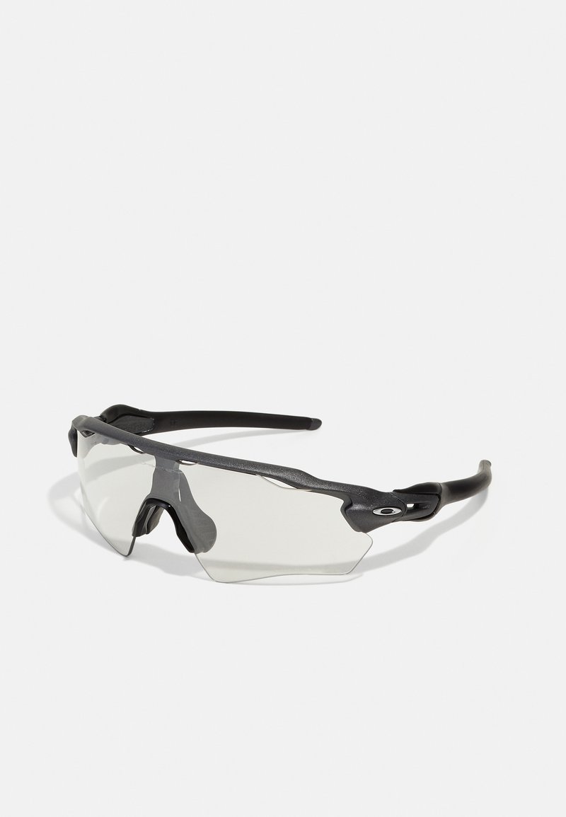 Sonnenbrille mit einem schwarzen Kunststoffrahmen, Wrap-Around-Design und klaren Gläsern. Bemerkenswerte Merkmale sind strukturierte Akzente und flexible Ohrpolster.
